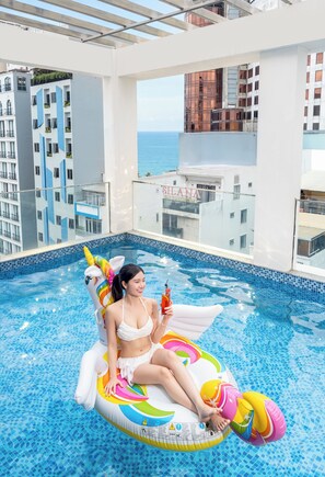Una persona seduta su un gonfiabile a forma di unicorno colorato in una piscina con vista sulla città.