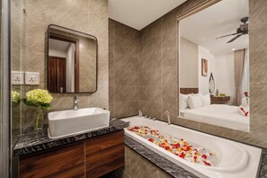 Un baño moderno con un espejo grande, un lavamanos rectangular y una bañera con pétalos de rosa.