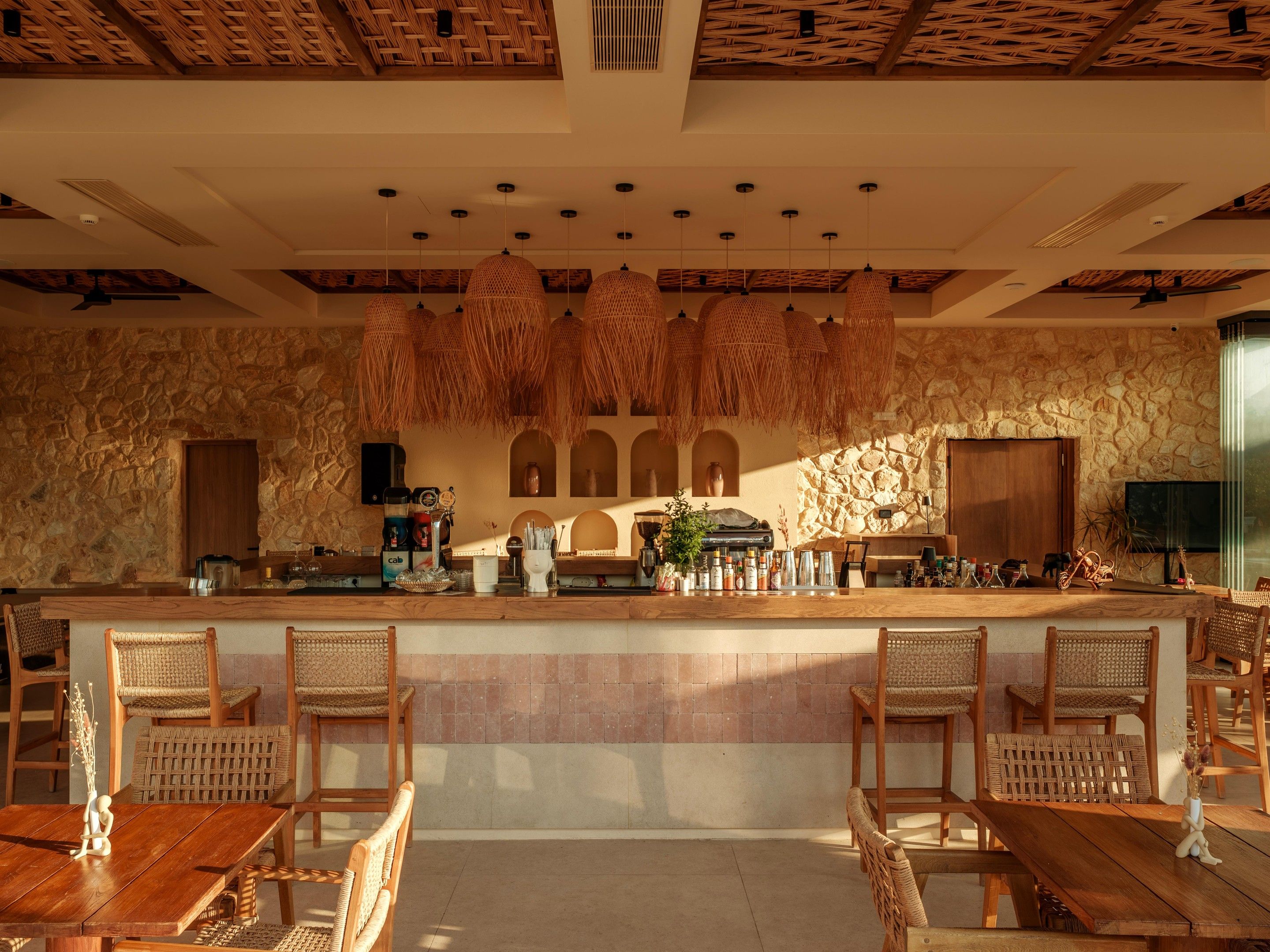 Un restaurante con pared de piedra, luminarias de techo tejidas y mobiliario de madera.