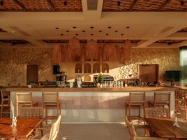 Un restaurante con pared de piedra, luminarias de techo tejidas y mobiliario de madera.
