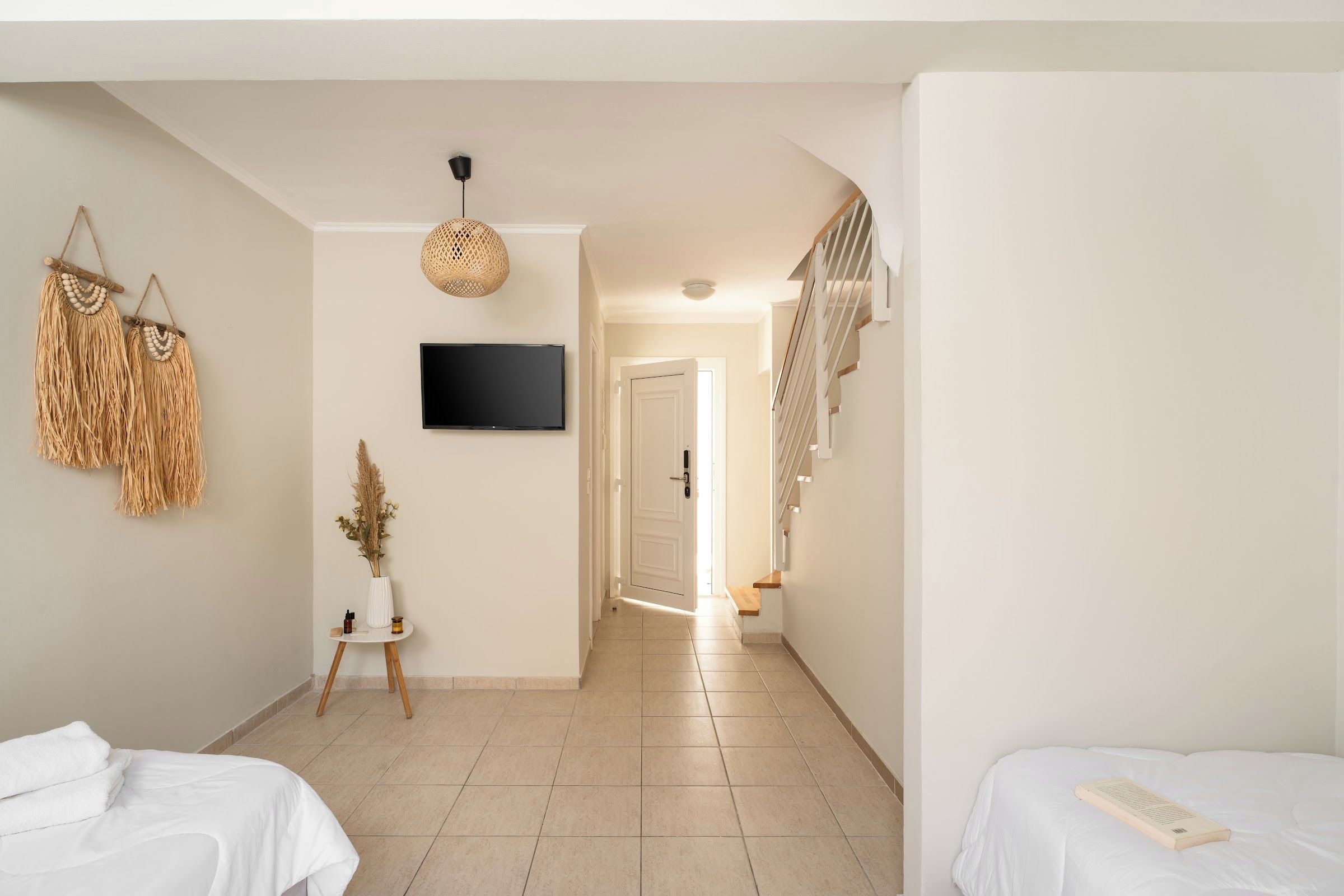 A hotel room with a bed, a bedside table, a TV, and a hallway leading to a staircase.