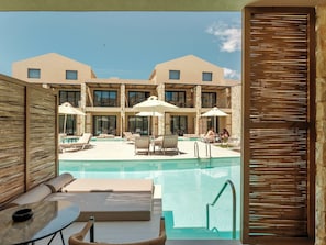 A pool area with lounge chairs, umbrellas, and a view of a building with multiple windows. - Ekati Mare Lifestyle Resort (Corfu)