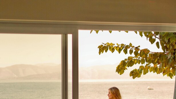 Une femme vêtue d’un bikini rouge, debout sur un balcon donnant sur la mer.