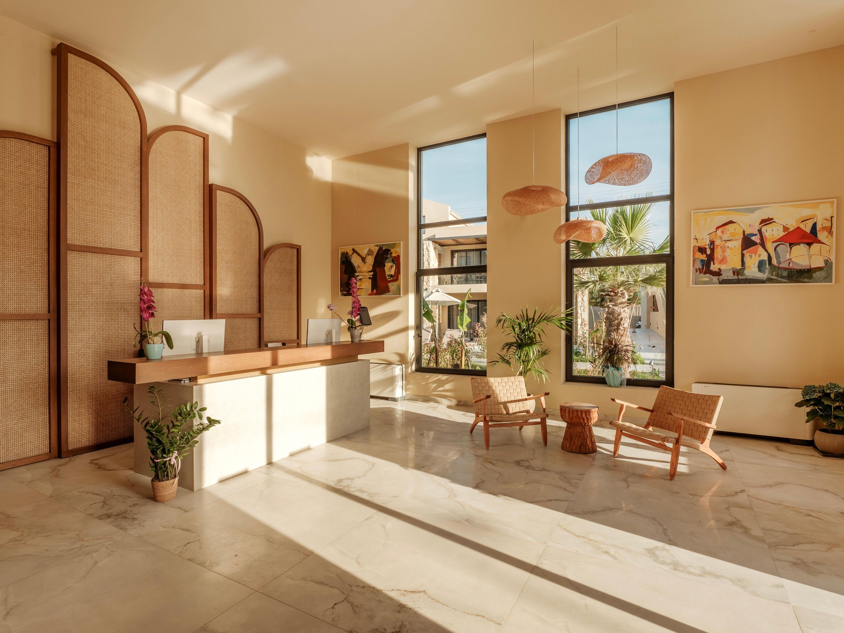 A reception area with a wooden reception desk, two wicker chairs, a marble floor, and large windows with views of the outside.
