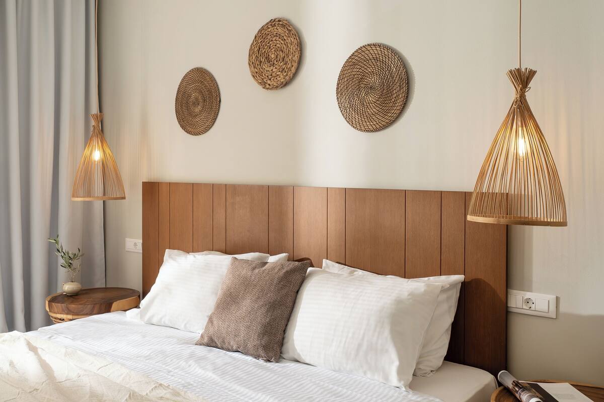 Ein ordentlich bezogenes Bett mit weißen Laken und einem braunen Kopfkissen, ein Holz-Kopfbrett und drei gewebte Wandbilder.