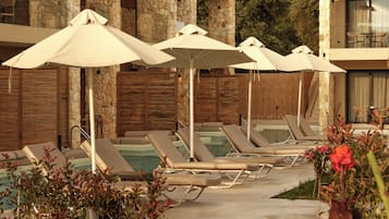 A poolside area with lounge chairs and umbrellas, stone walls, and a wooden fence.