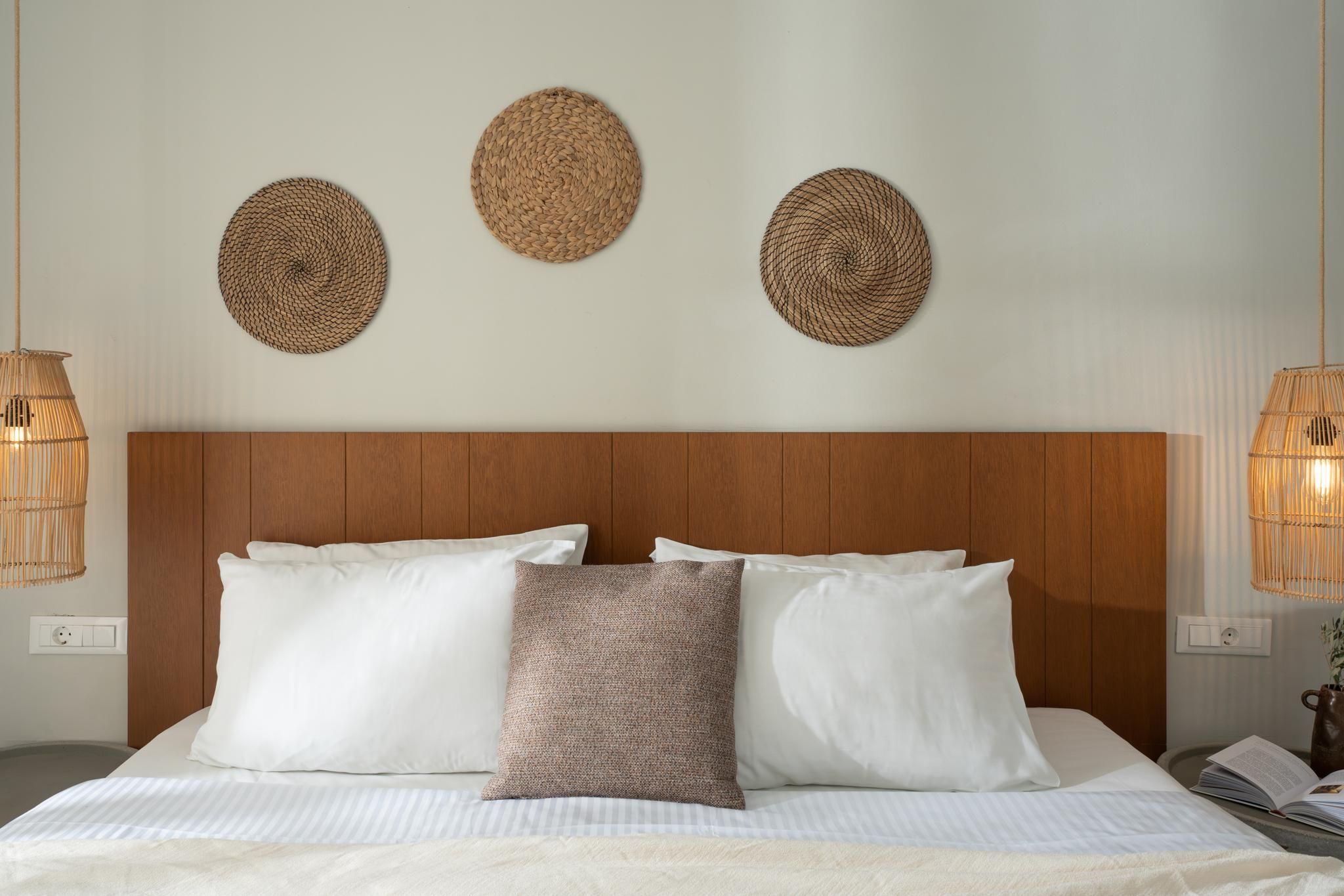 Ein Hotelzimmer mit einem Holzkopfteil, einem Bett mit weißen und gemusterten Kissen sowie drei gewebten Wanddekorationen.