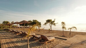 Un complexe hôtelier situé en bord de mer, doté d’une terrasse en bois avec des sièges, de palmiers et offrant une vue sur l’océan.