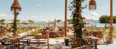 Een terras met tafels en stoelen, parasols en uitzicht op zee.