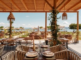 Un área de comedor al aire libre con mesas, sillas, sombrillas y vista al mar.