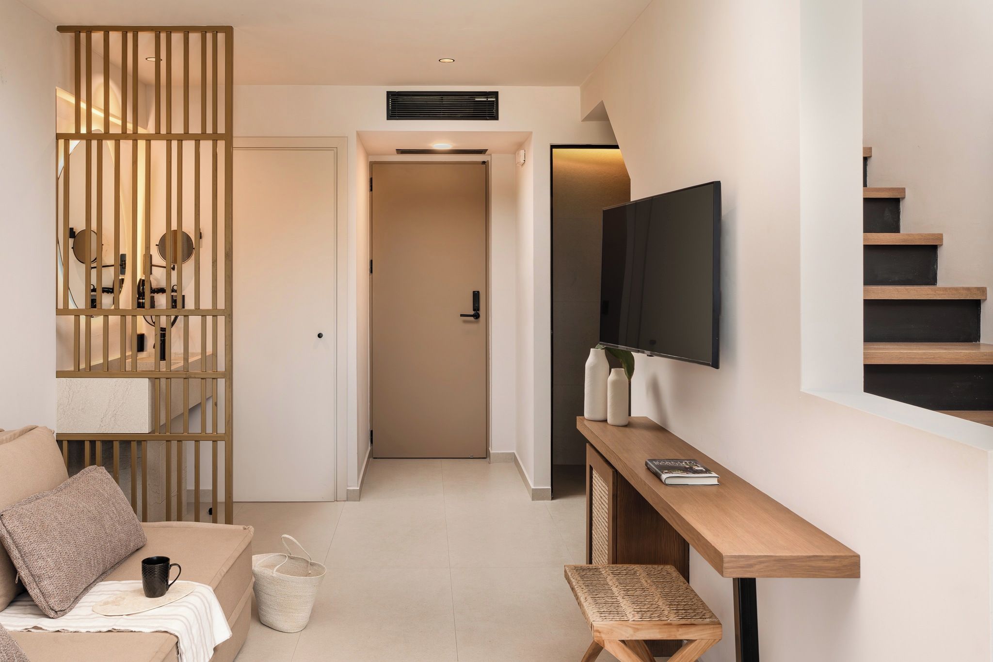Una sala de estar moderna con un sofá, una mesa de centro, un televisor montado en la pared y una escalera que sube a otro nivel.
