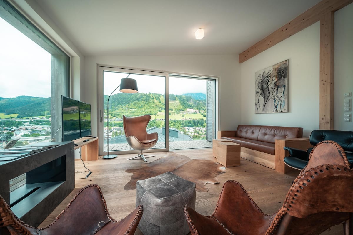 Una sala de estar moderna con un ventanal grande, un televisor de pantalla plana, muebles de cuero y un cuadro en la pared.
