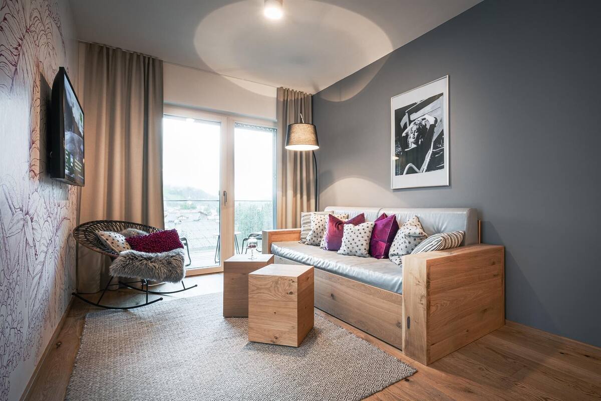 Una sala de estar moderna con un sofá, un sillón mecededor, una mesa de centro y un ventanal grande.