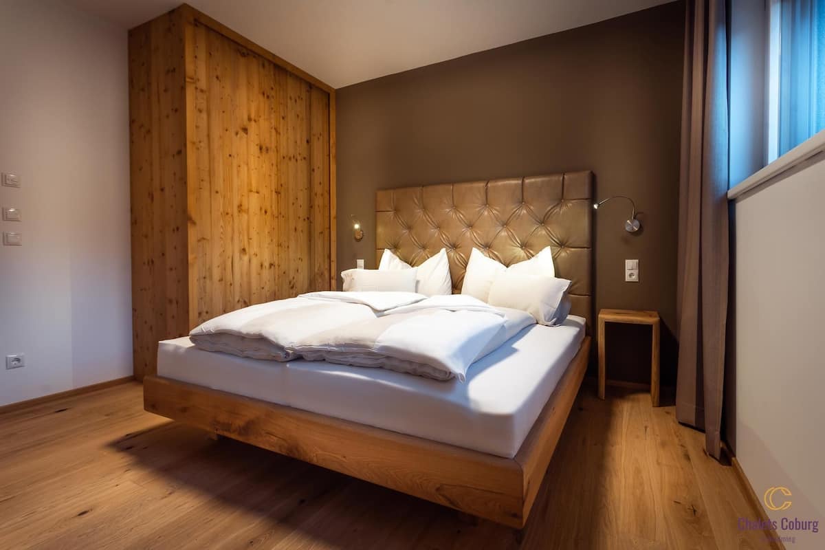 Un dormitorio moderno con piso de madera, una cama grande con cabecera capitonada y una mesita de noche.