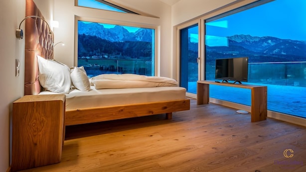 A modern bedroom with a wooden bed, large windows, and a TV. - Boutique Aparthotel Chalets Coburg (Schladming)