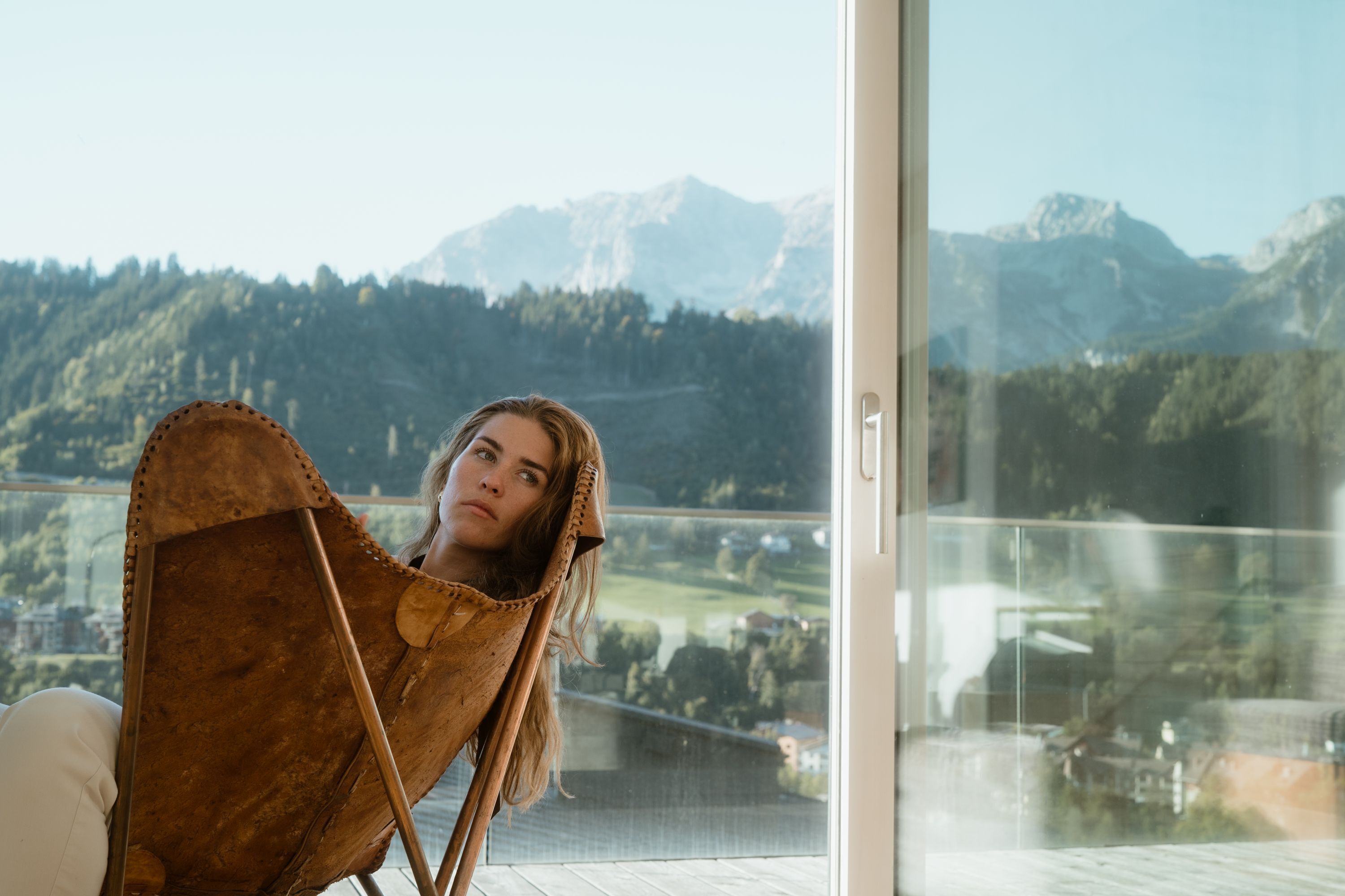 Una persona sentada en una silla con vista a un paisaje montañoso a través de un ventanal.
