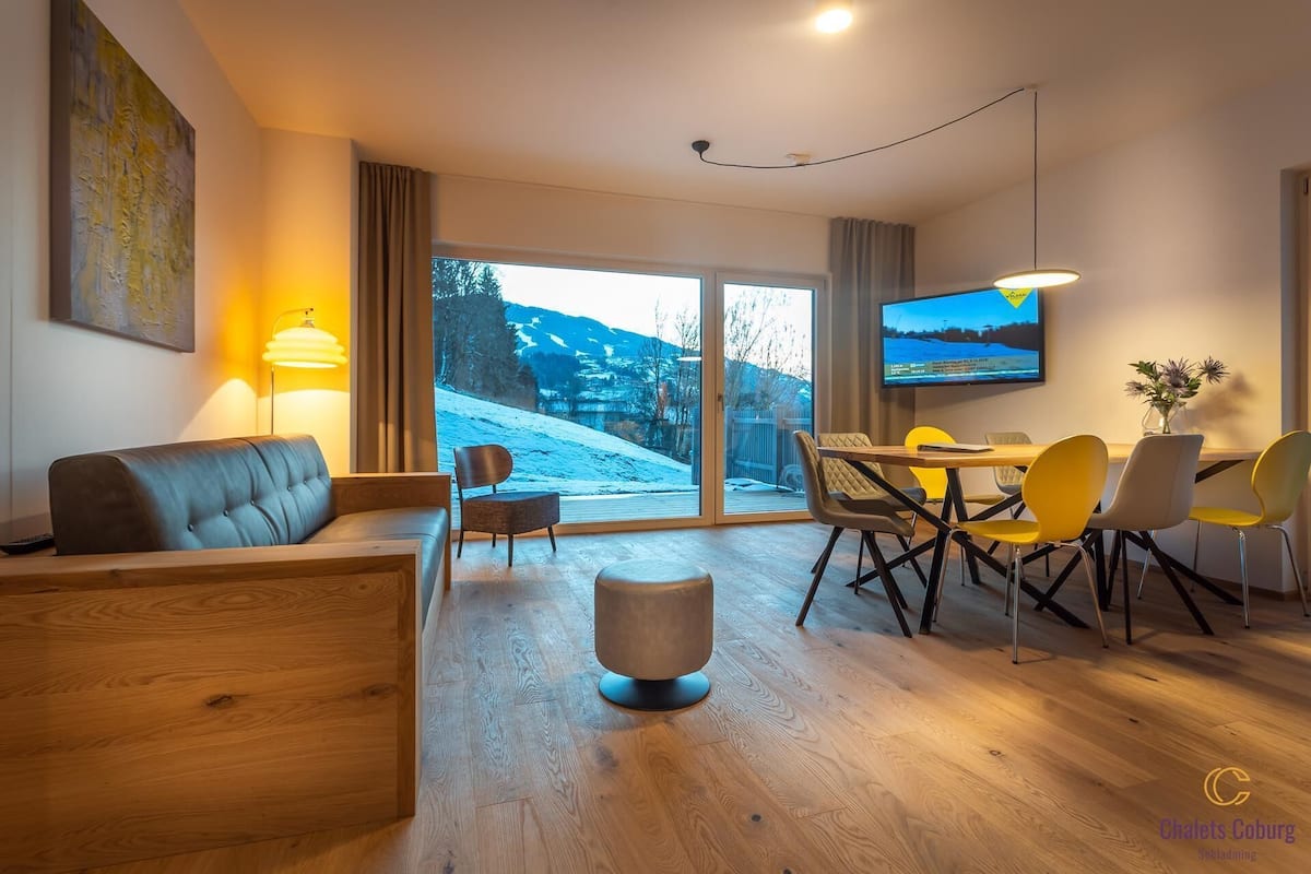 Una sala de estar moderna con sofá, sillas, mesa de comedor y televisor.