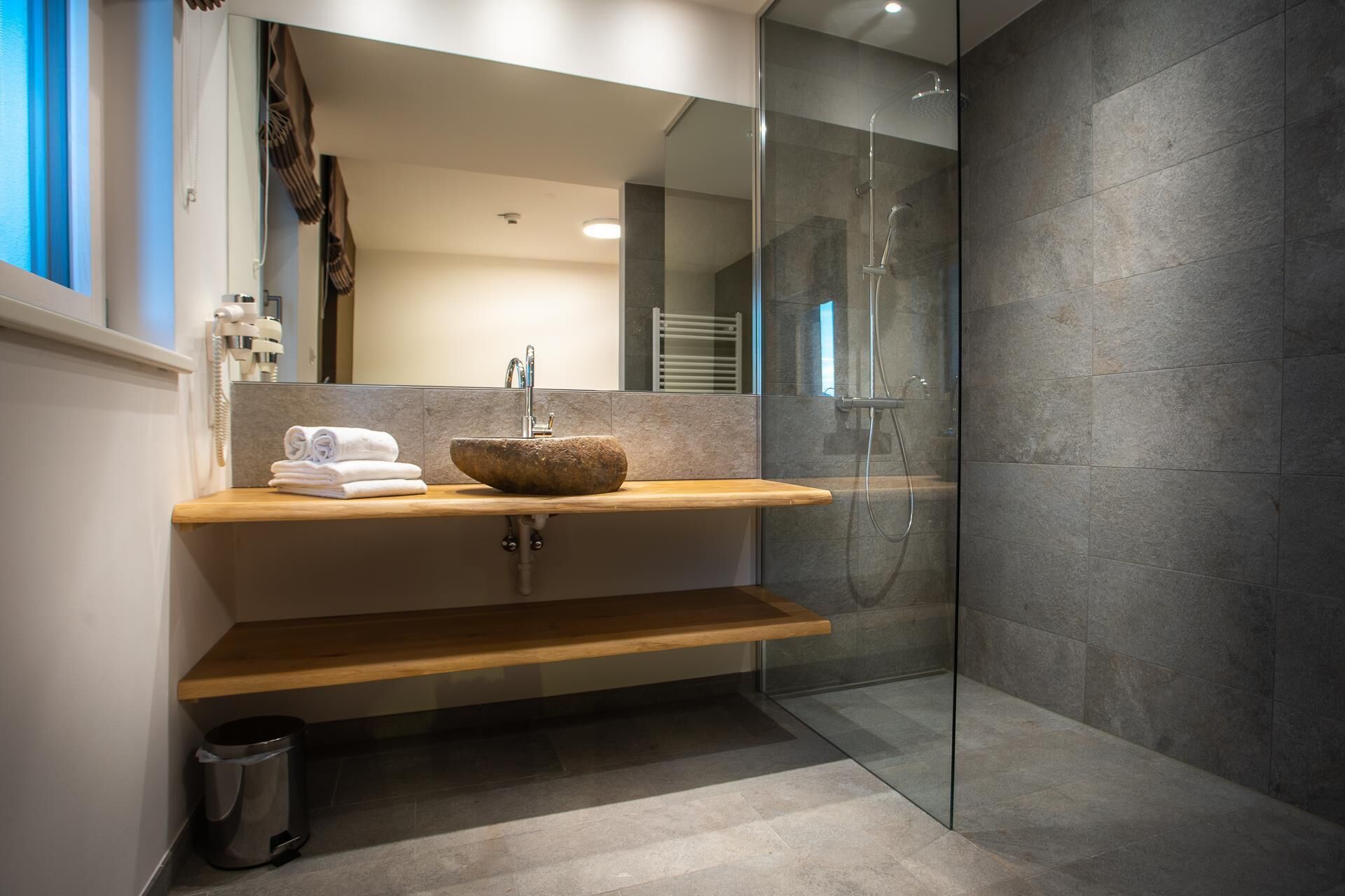 A modern bathroom with a stone sink, a glass-enclosed shower, and a wooden vanity.