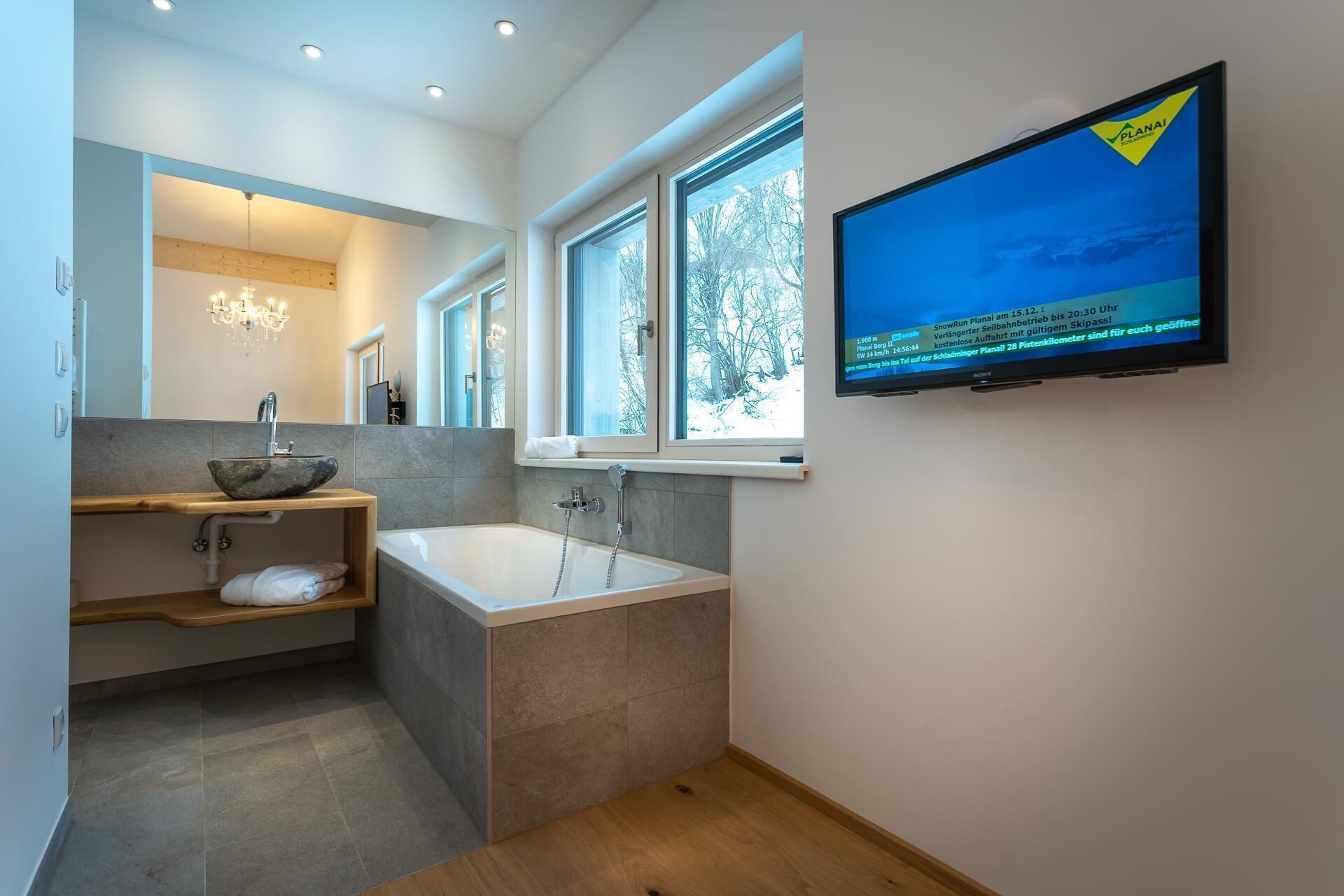 Ein modernes Badezimmer mit einer freistehenden Badewanne, einem großen Spiegel und einem an der Wand montierten Fernseher.