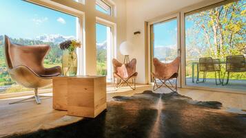 Ein modernes Interieur mit großen Fenstern, Ledersesseln, einem Holztisch und einem schwarzen Lederteppich.