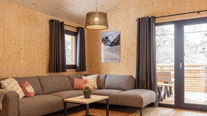 Un salon moderne avec un canapé d’angle, une petite table sur laquelle est posé un vase, et une grande fenêtre avec des rideaux.