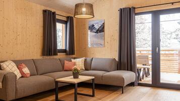 Ein modernes Wohnzimmer mit einer Eckcouch, einem kleinen Tisch mit einer Vase und einem großen Fenster mit Vorhängen.