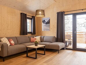A modern living room with a sectional sofa, a small table with a vase, and a large window with curtains. - Superior mit Sprudelbad innen by Interhome (Turracher Höhe)