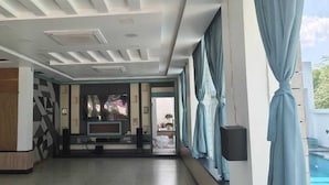 Een moderne hotel lobby met een groot televisiescherm, een houten accentmuur en uitzicht op het omliggende landschap.
