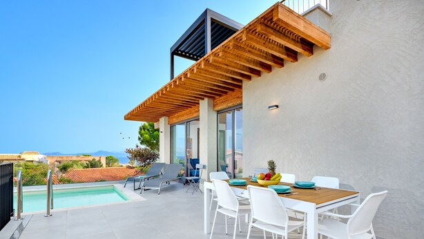 Uma área de refeições moderna ao ar livre, com piscina, cadeiras brancas e uma pérgola de madeira.