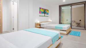 Quarto de hotel com duas camas, uma porta de correr de vidro, uma obra de arte colorida e uma pequena varanda.