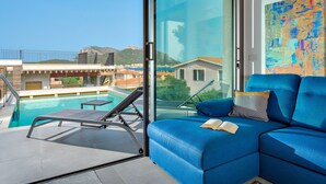 Uma sala de estar moderna com uma grande janela de vidro, um sofá azul e vista para a piscina.