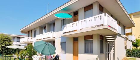 A two-story building with balconies, a fenced patio area, and outdoor seating.