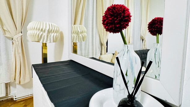 Une salle de bain avec un plan de toilette noir, un lavabo blanc, un miroir et un vase contenant des fleurs rouges.