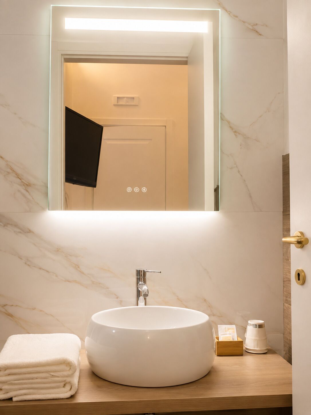 A bathroom with a marble sink, a mirror with a light, and a towel on the counter.