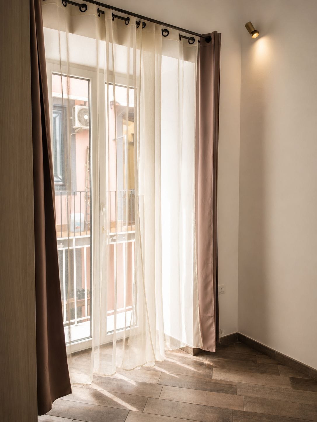 A room with a sliding glass door, a wooden floor, and a wall-mounted light fixture.
