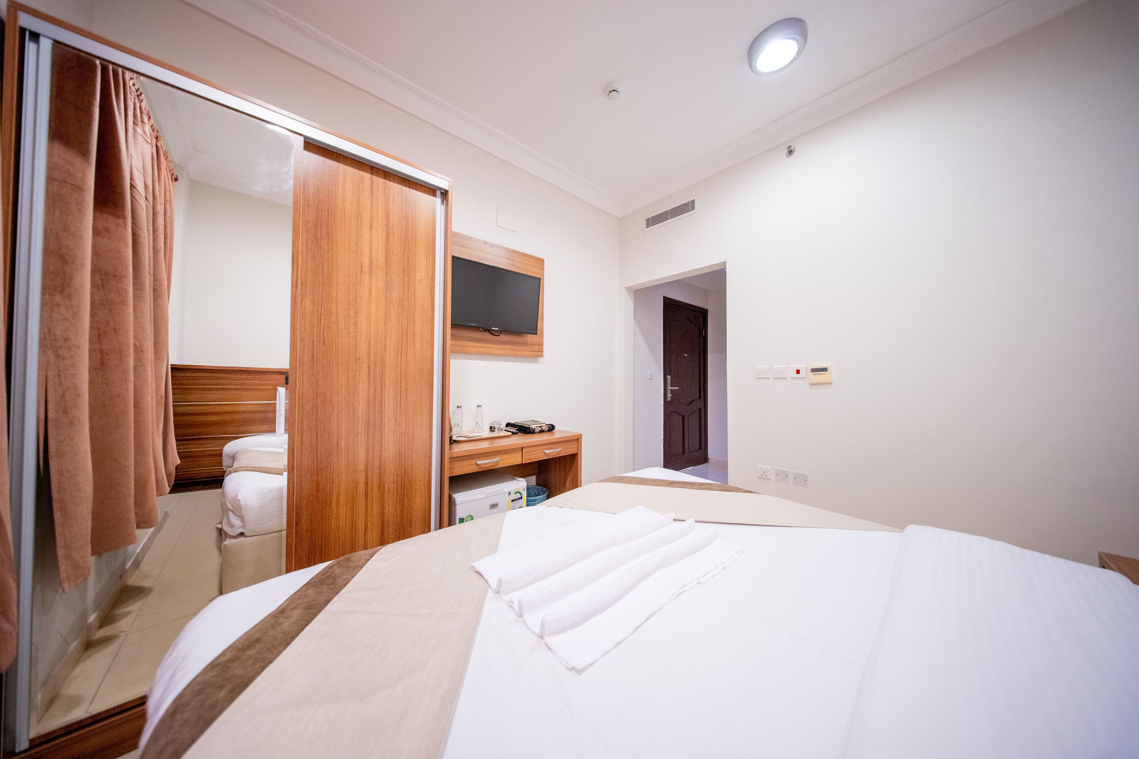 A hotel room with a bed, a wooden wardrobe, a desk with a flat-screen TV, and a bathroom with a mirror and towel rack.