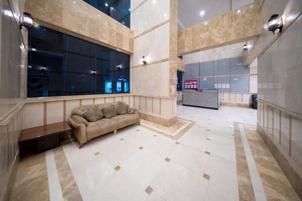 A spacious lobby with a plush sofa, a reception desk, and a large window offering a view of the interior.