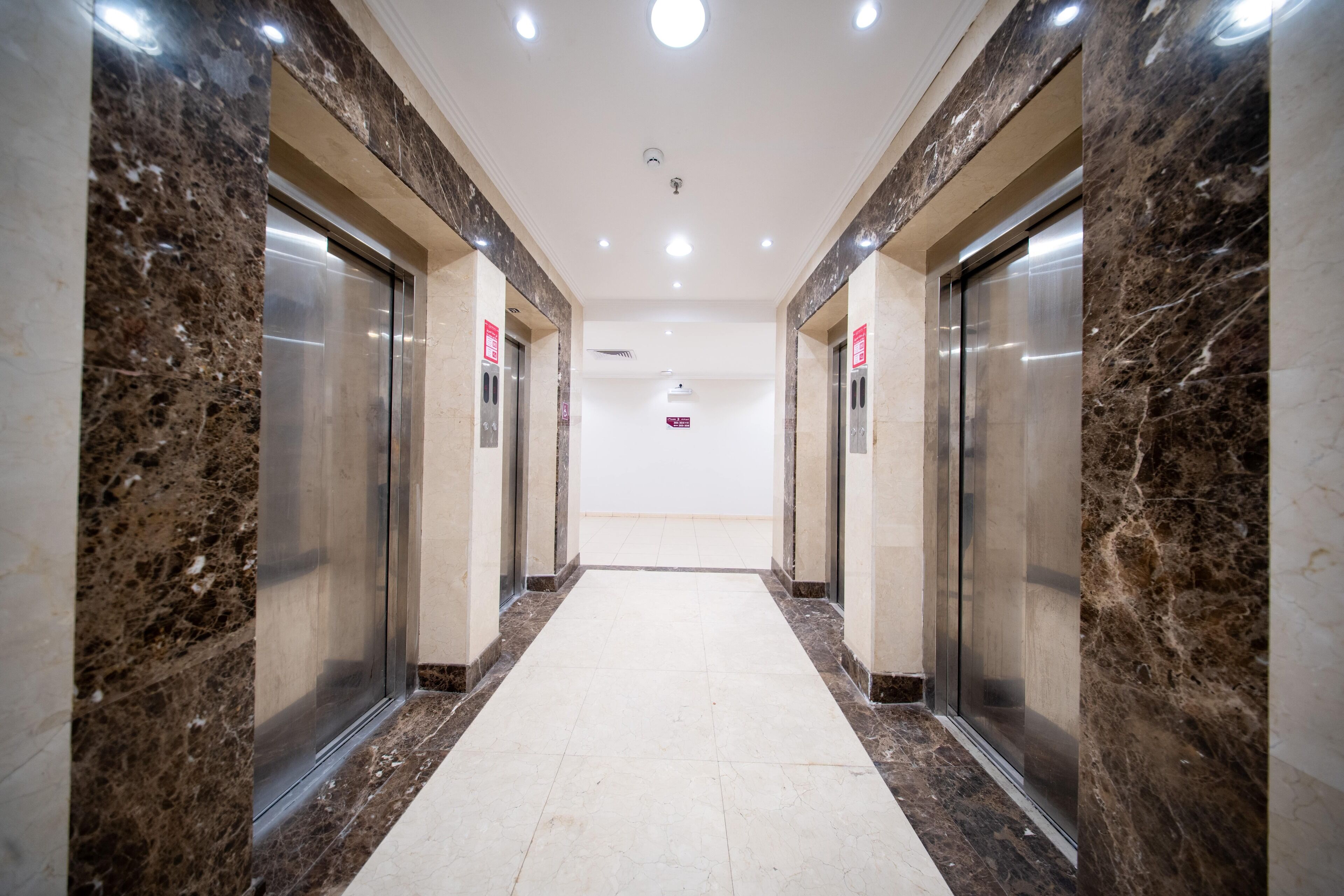 Corredor com paredes de mármore e dois elevadores.