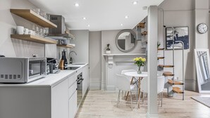 Een moderne keuken met witte kasten, een eethoek met een witte tafel en stoelen, en een trap met houten treden.
