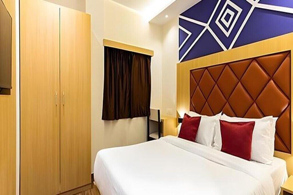 A hotel room with a large bed, a wardrobe, a window with curtains, and a decorative wall panel.