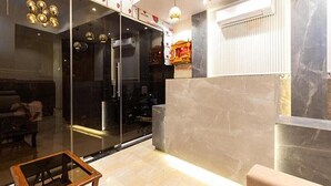 Um hall moderno com divisória de vidro, balcão de recepção em mármore e área de estar com sofá e uma mesa pequena.