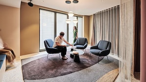 Une chambre d’hôtel moderne dotée d’une grande fenêtre, d’une table basse ronde, de deux fauteuils et d’un tapis à motifs.
