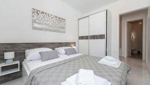 Moderni hotellihuone, jossa on suuri sänky, yöpöytä, seinälle ripustettu taideteos ja liukuovilla varustettu vaatekaappi.