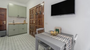A small room with a kitchenette, a dining table with a patterned tablecloth, and a flat-screen TV mounted on the wall. - Vacation Studio 'Tagoro' with Wi-Fi (Guía de Isora)
