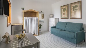 A living room with a sofa, a table with a decorative bowl, a television, a mirror, and framed pictures on the wall. - Vacation Studio 'Tagoro' with Wi-Fi (Guía de Isora)