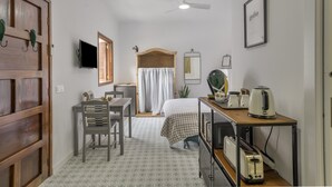 A small, well-lit room with a bed, a desk with a chair, a television, a ceiling fan, and a framed picture on the wall. - Vacation Studio 'Tagoro' with Wi-Fi (Guía de Isora)