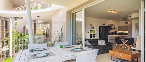 An open-plan living area with a dining table, chairs, a sofa, and a kitchen in the background.