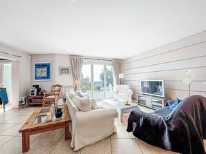 Ein Wohnzimmer mit Sofa, Couchtisch, Fernseher und Blick ins Freie.