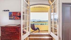 Een kamer met een houten dressoir, een stoel en uitzicht op een landelijk landschap door open deuren.