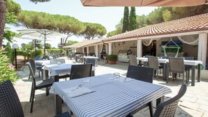 An outdoor patio area with tables and chairs, a covered seating area, and a view of trees and a building in the background. - Bungalow Superior by Interhome (Capalbio)